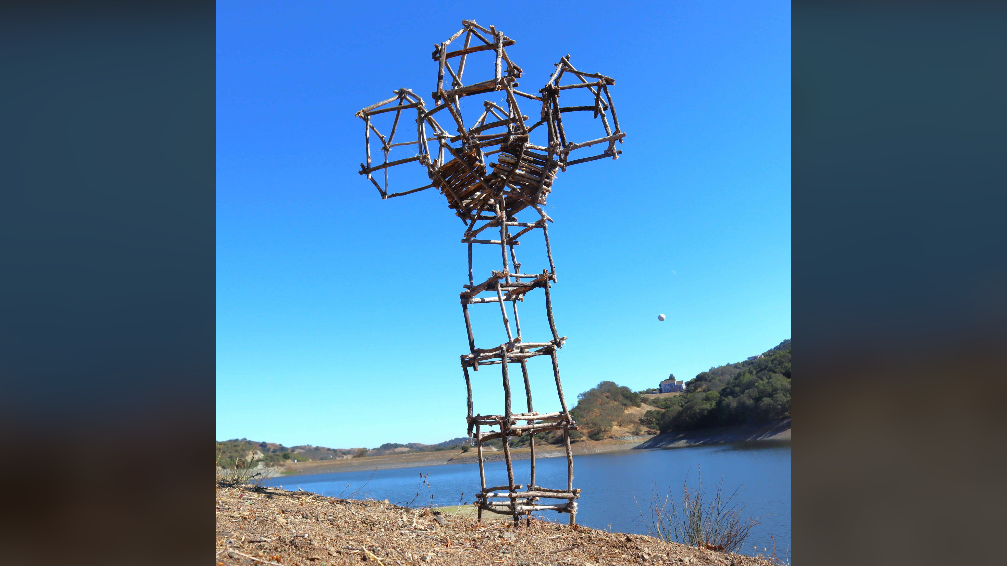 Full view of the sculpture built beside a lake against a bright blue sky.