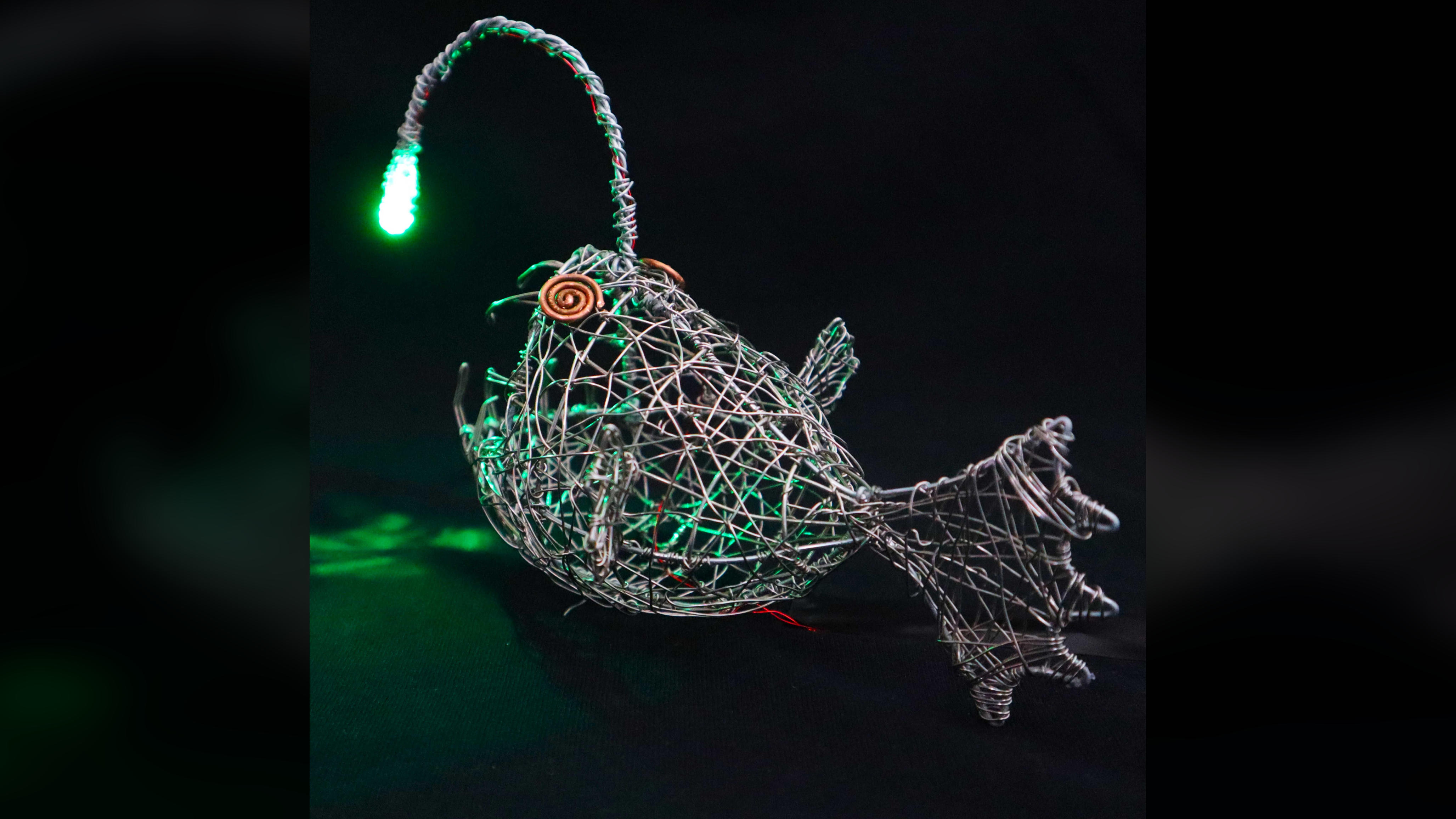 Back view of the wire anglerfish sculpture illuminated by its green LED.