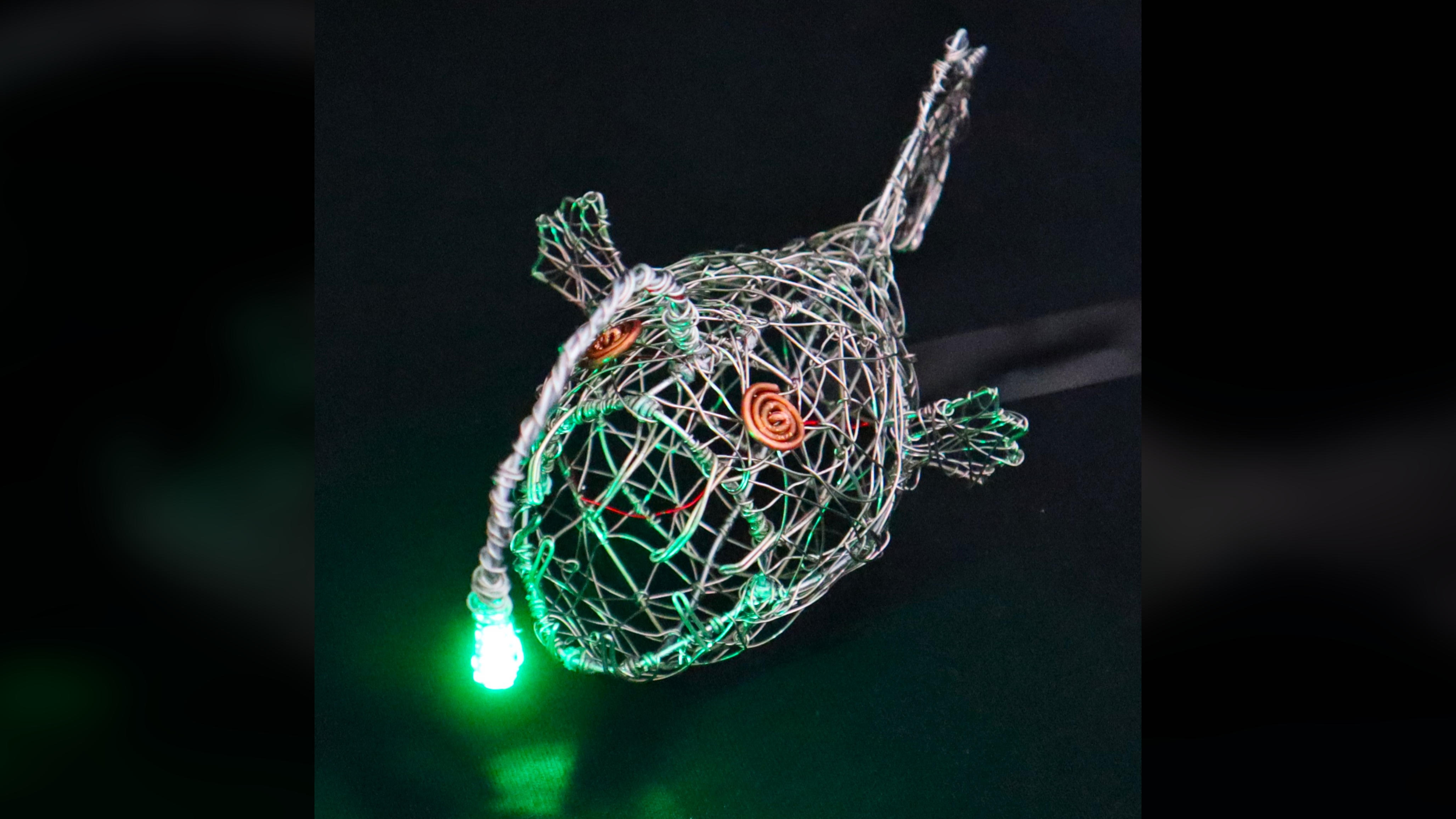 Close-up front view of the wire anglerfish sculpture illuminated by its green LED.
